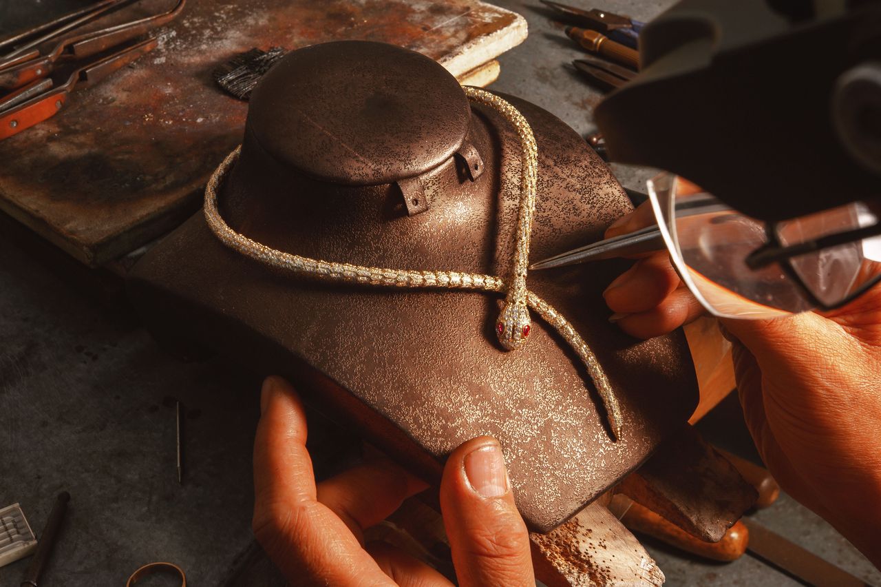 Jewelry artisan meticulously crafting a gold snake necklace in a traditional workshop setting.
