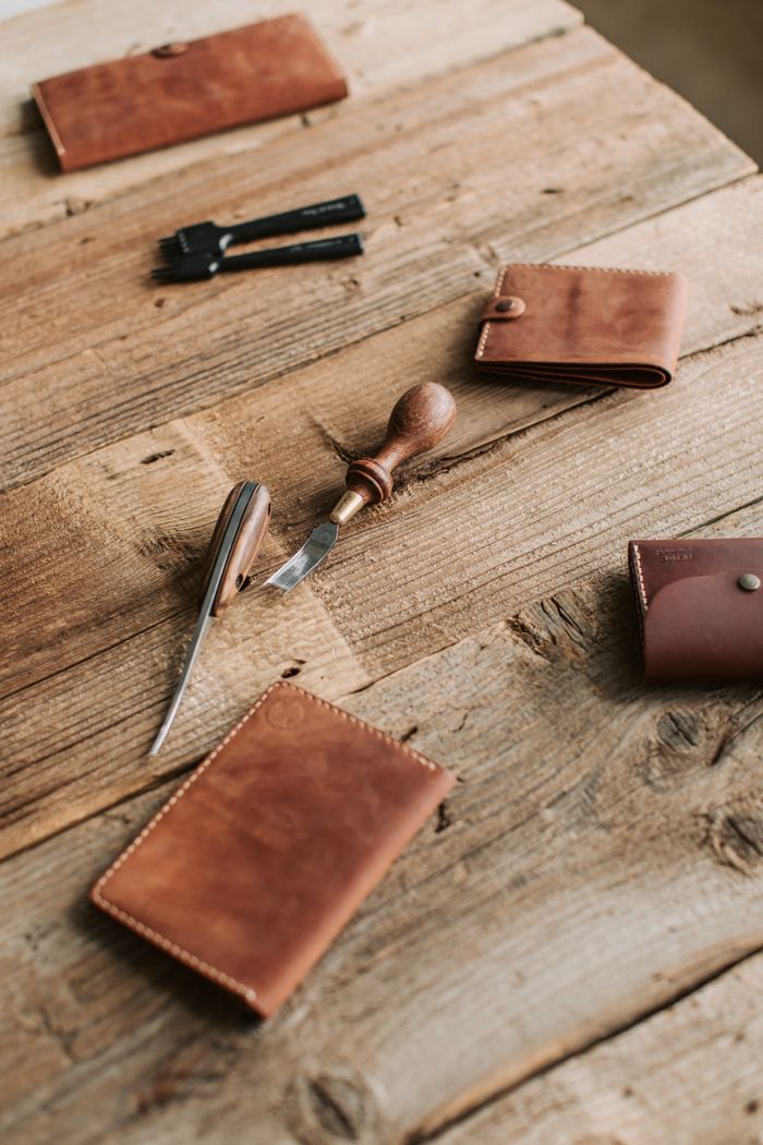 Artisanal leather wallets with crafting tools on a rustic wooden table, showcasing craftsmanship.